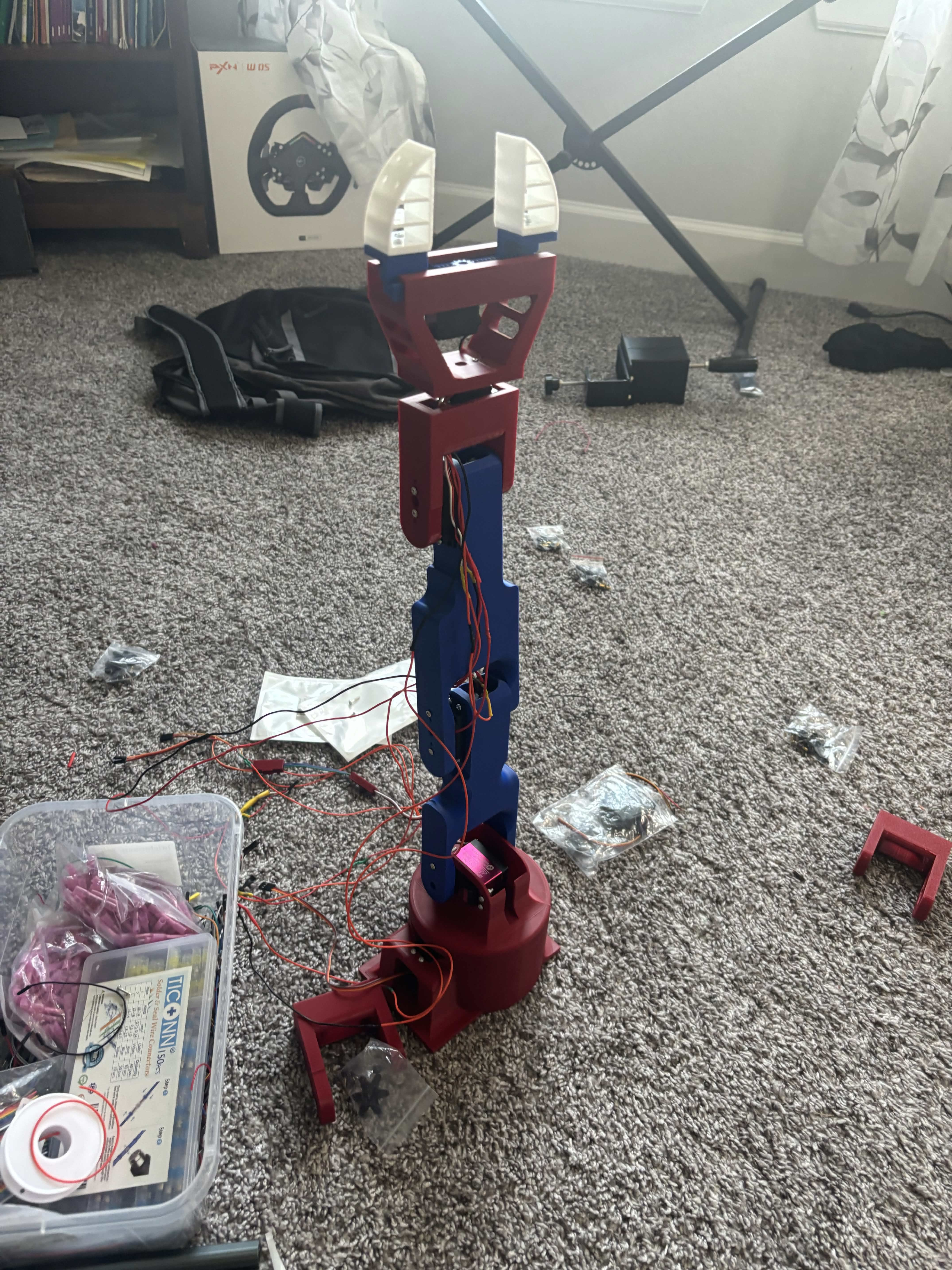 An upright assembled robotic arm prototype with wiring connected to its red base and white gripper fingers