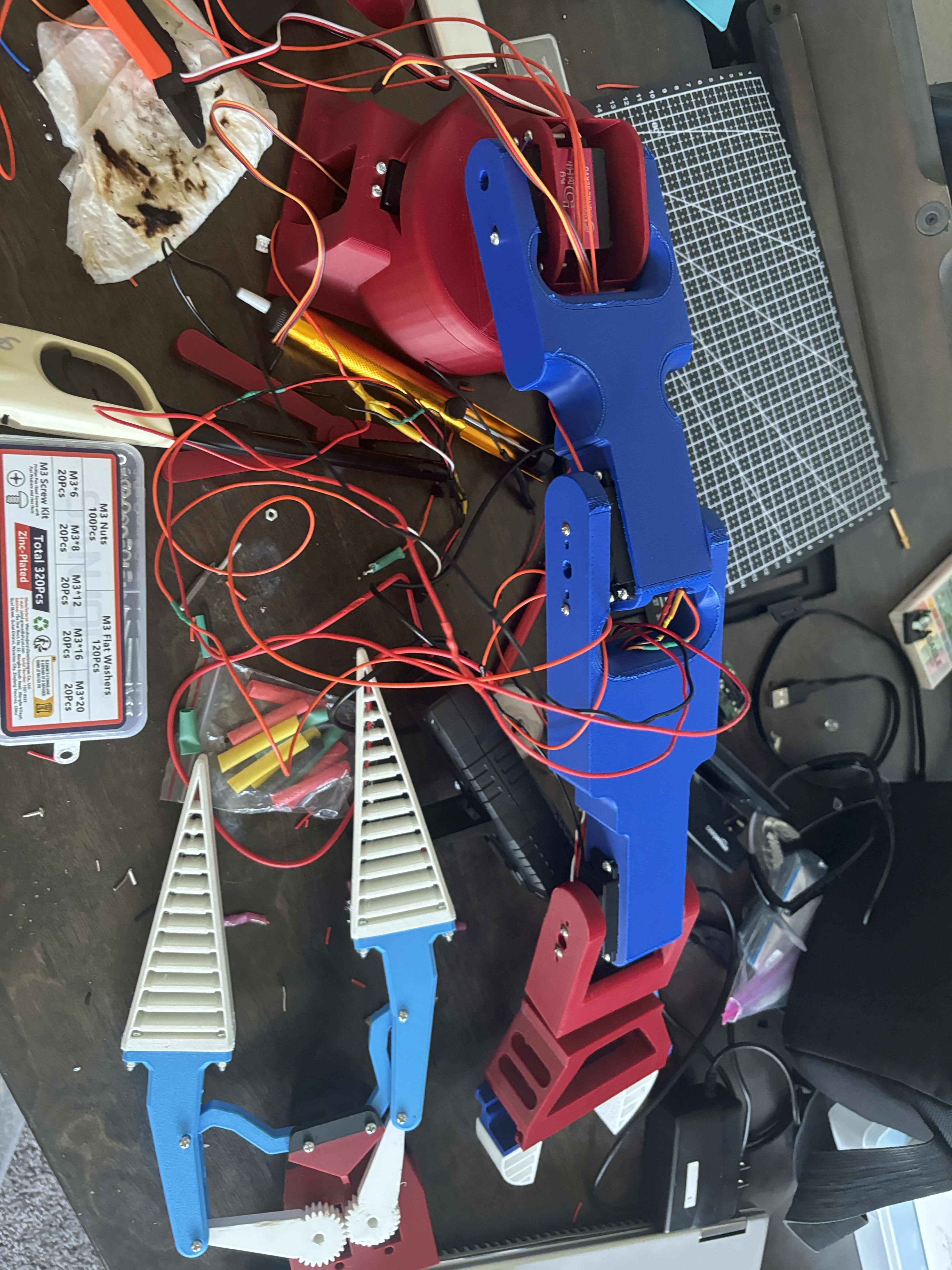 Top view of the robotic arm showing its linked blue segments, red mounts, white gripper fingers, servos, and wiring