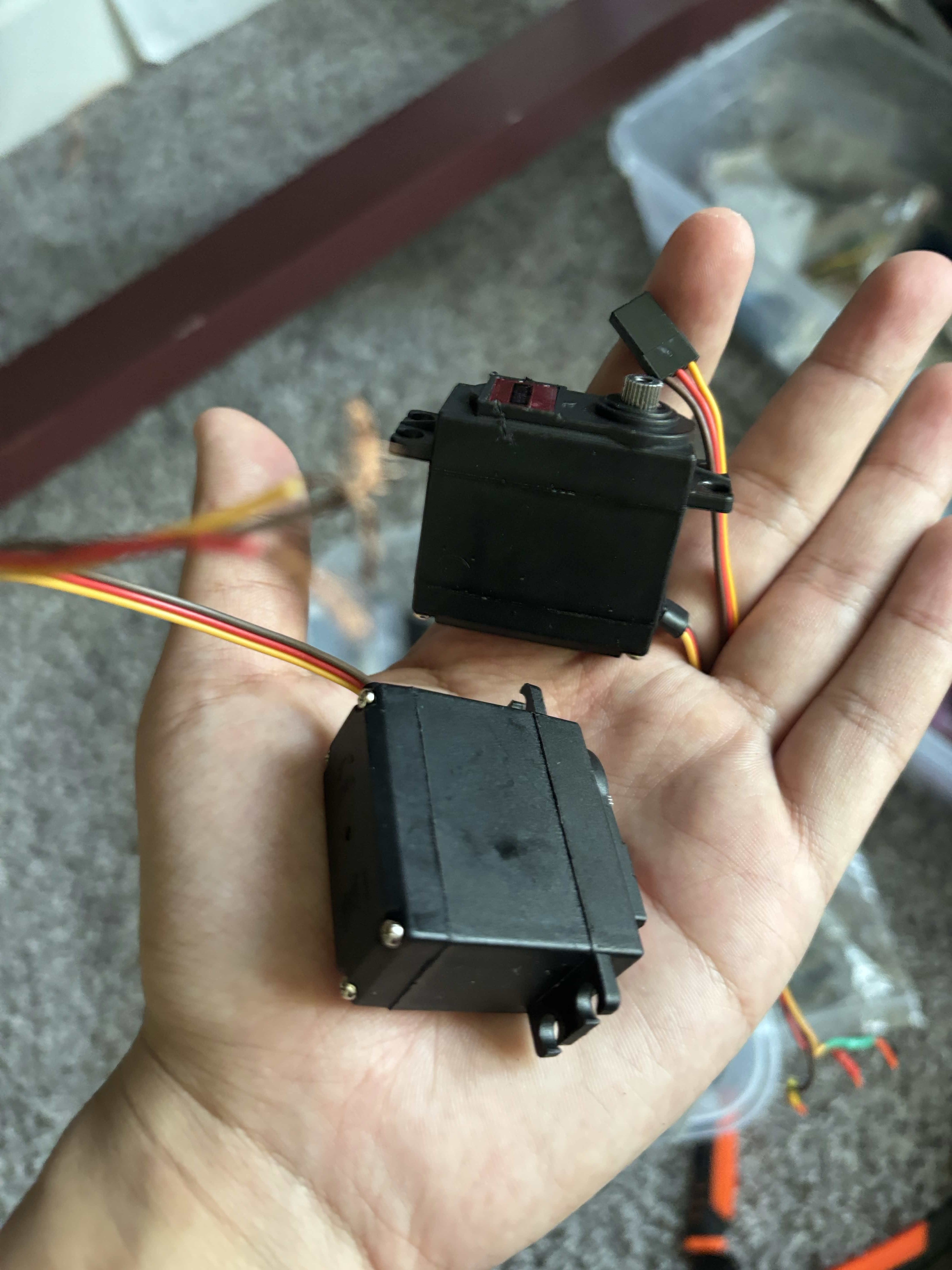 Two black metal-geared servo motors held in a hand