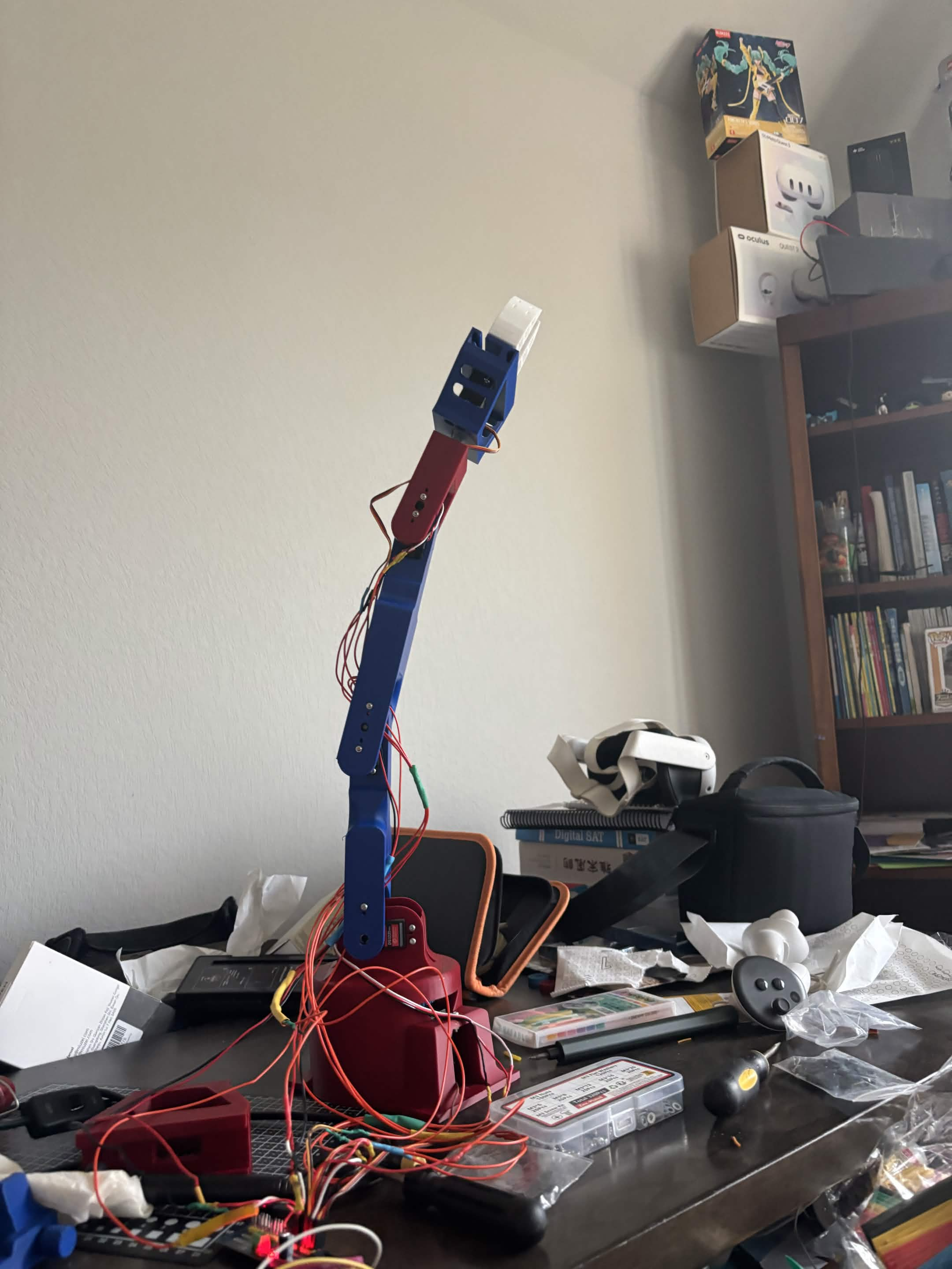 Tall blue and red robotic arm standing upright on a desk with its wiring exposed